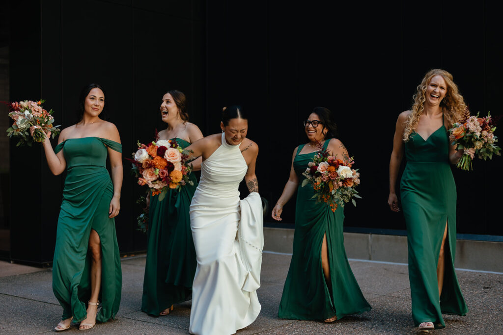 Bride stumbles over her dress while laughing with her bridesmaids