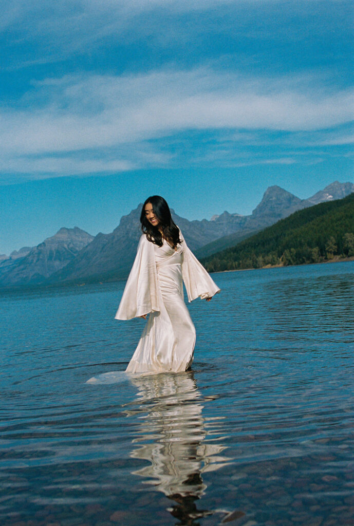 Bride wades through glacial waters in Glacier National Park for Yellowstone wedding in Montana.