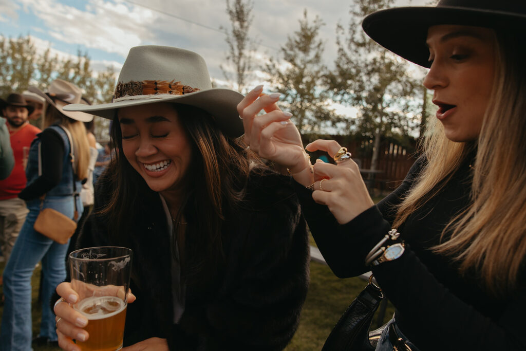 Bride laughs with friends at craft brewery welcome dinner. 