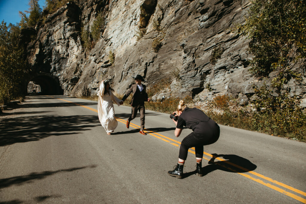 Traveling wedding photographer captures bride and groom running hand in hand down Montana highway. 