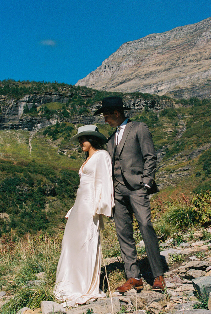 Bride and groom stand on rock overlooking Glacier National Park. 