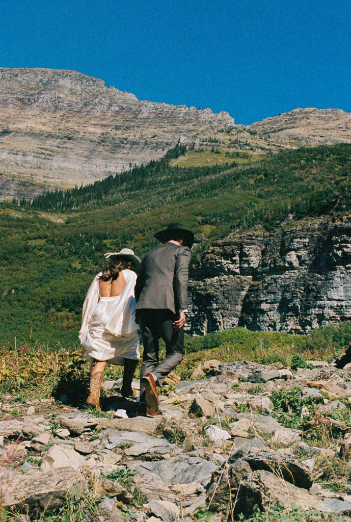 Bride and groom walk hand in hand through Glacier National Park. 