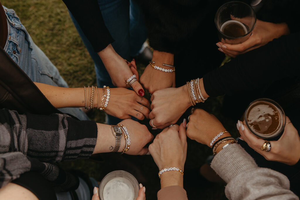 Hands holding craft beers show off their friendship bracelets.