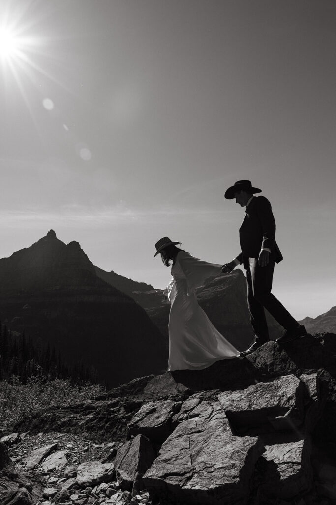 Bride and groom hold hands as they walk across rocks in Glacier National Park for Yellowstone wedding in Montana.