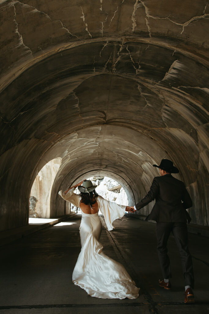 Bride and groom run hand in hand through tunnel in Glacier National Park.