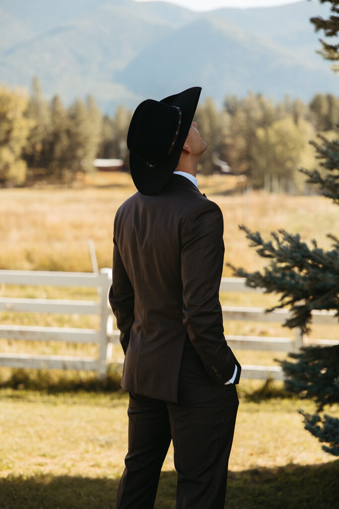 Groom in cowboy hat looks up at the sky as he waits to see his bride. 