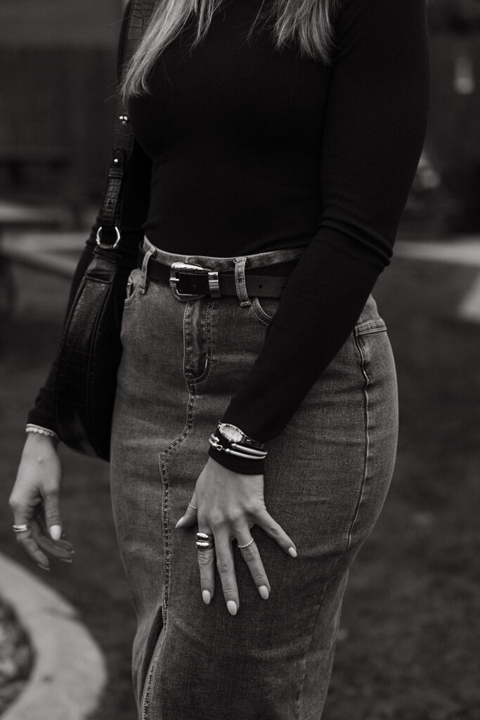 Woman in midi denim skirt and black turtleneck shows off her outfit. 