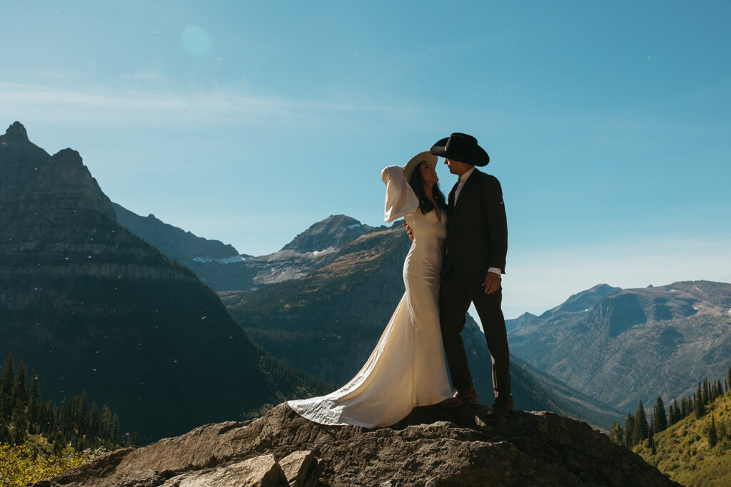 Bride and groom stand on rock overlooking the mountains in Glacier National Park for Yellowstone wedding in Montana.