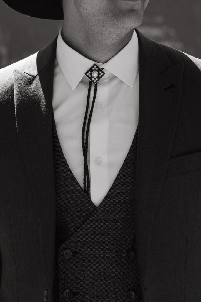 Groom wears bolo tie and sharp suit and cowboy hat. 