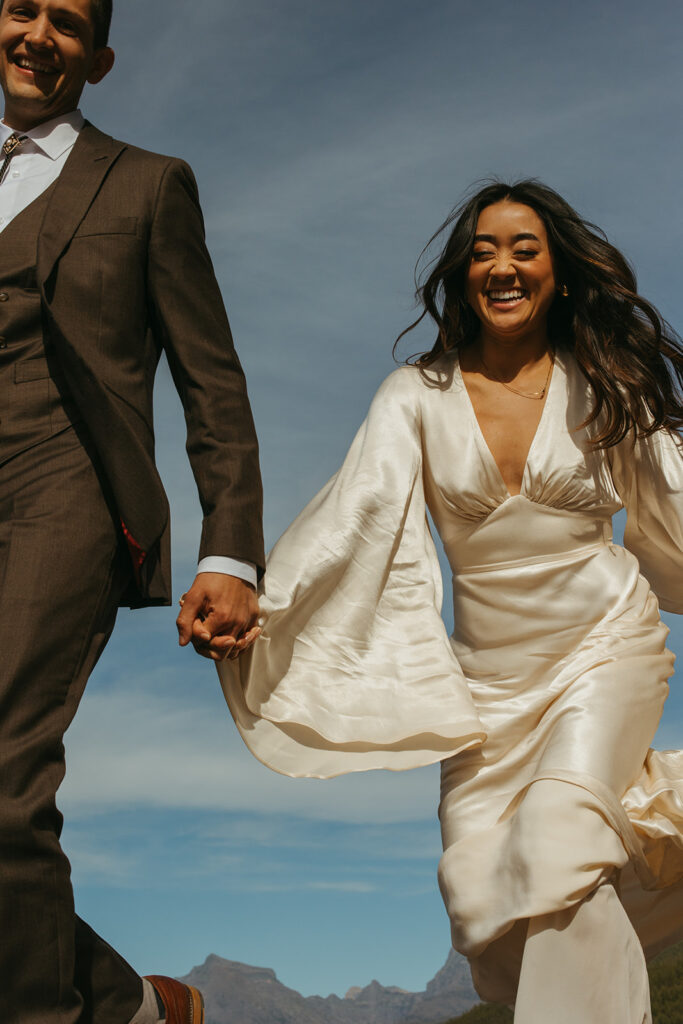 Bride and groom run hand in hand in Glacier National Park for their Yellowstone wedding. 