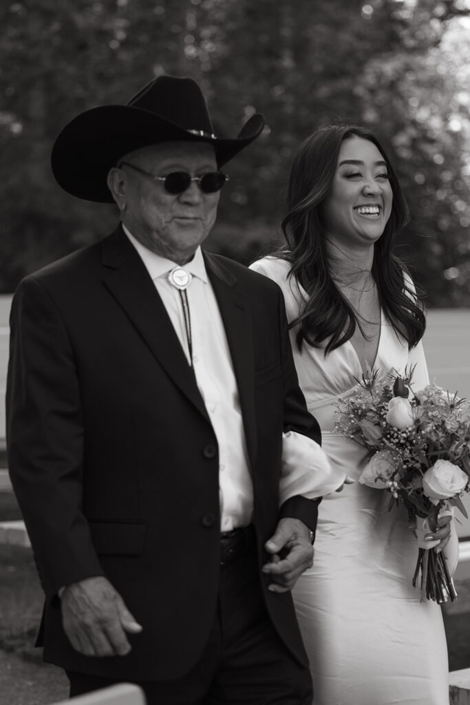 Bride walks down the aisle with her father with a big smile on her face. 