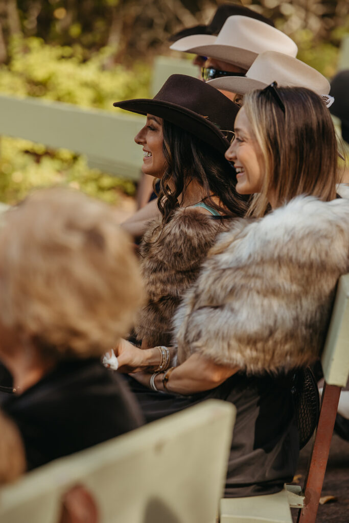 Wedding guests wearing fur coats and cowboy hats in Yellowstone wedding look on as bride and groom say their vows. 