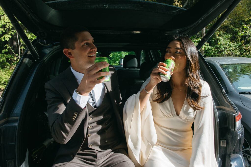 Bride and groom enjoy a celebratory beer in the boot of their car after their ceremony. 