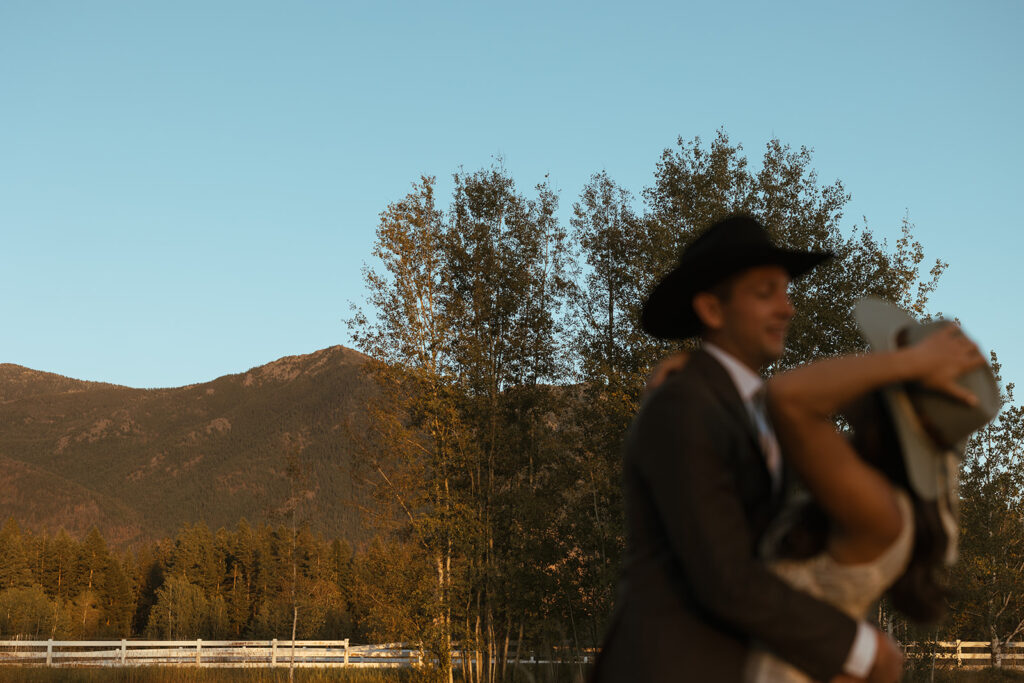 Bride and groom embrace in the foreground with mountain in the background