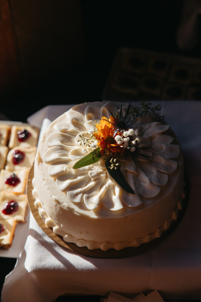 Wedding cake topped with wildflowers sits in sunlight. 