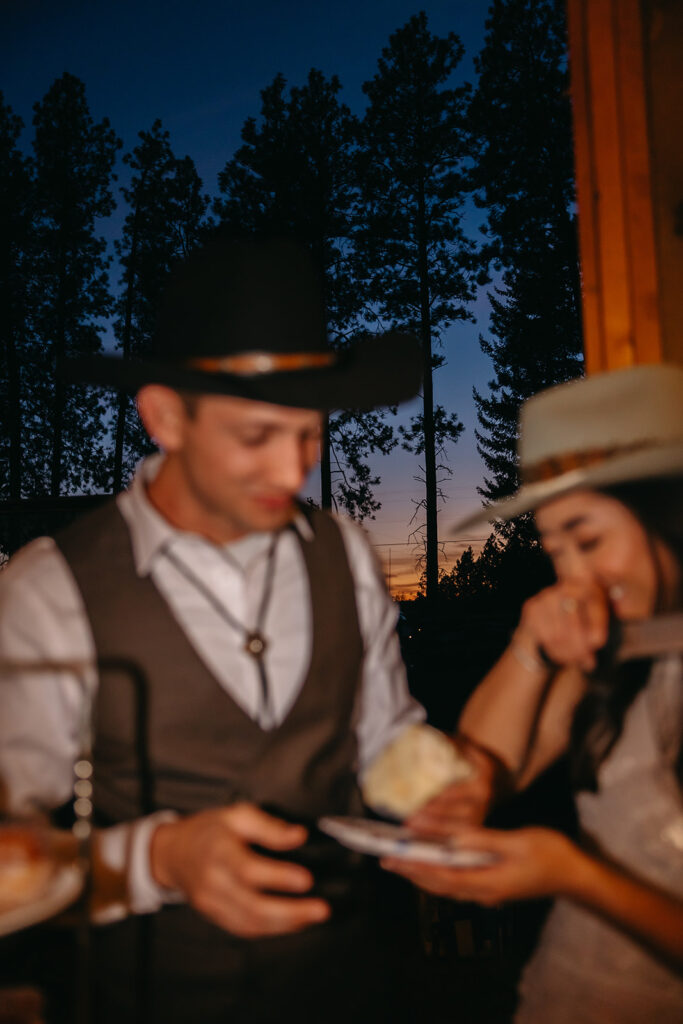 Bride and groom enjoy a bite of their wedding cake while the sun sets behind them