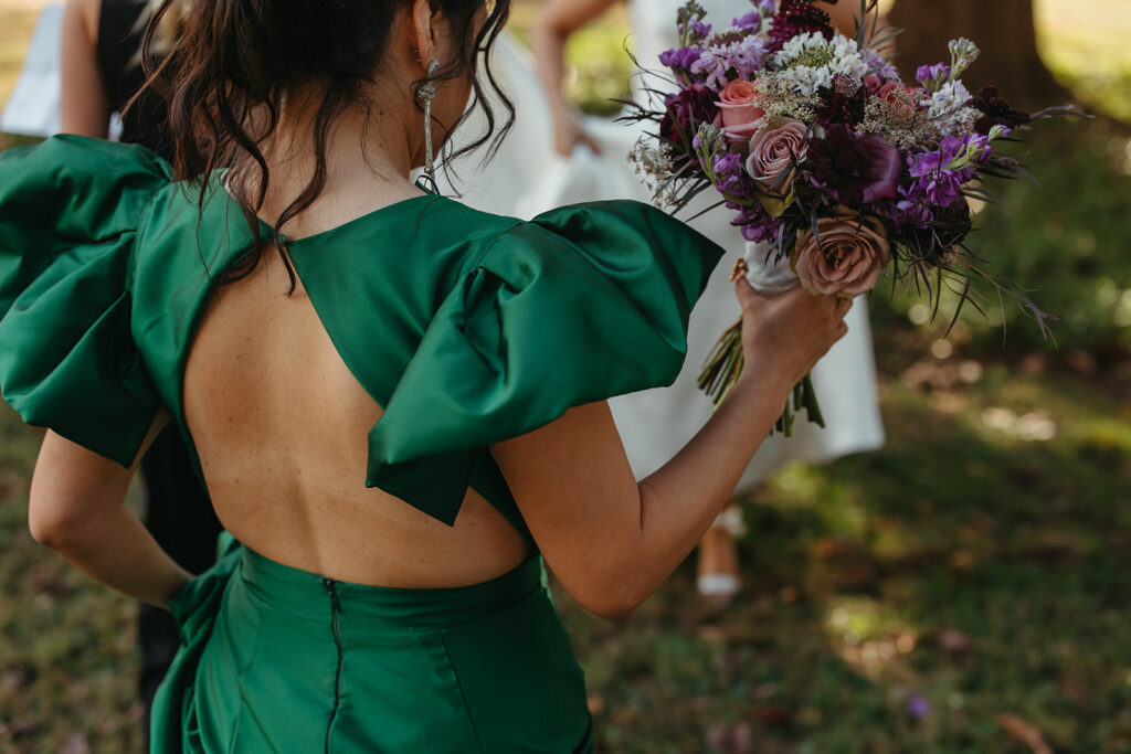 Wedding guest wearing chic emerald green gown carries bridal bouquet during black tie wedding in Nashville