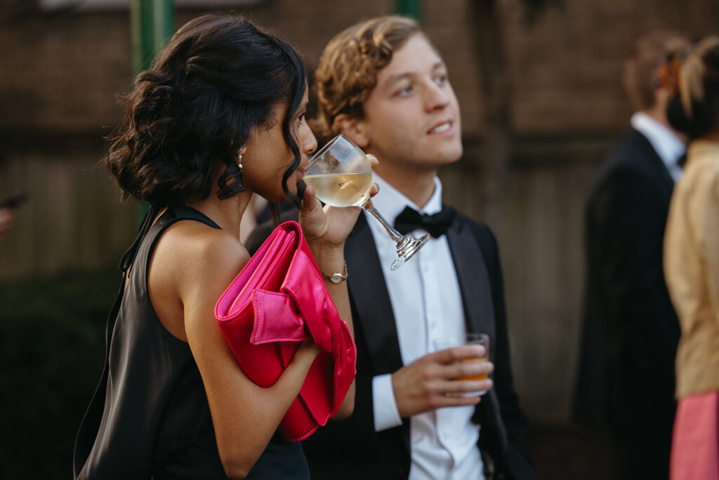 Chic woman carrying hot pink handbag sips from glass of white wine