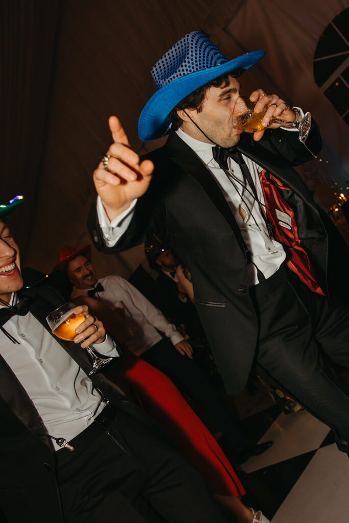 Wedding guest holds a finger in the air as he takes a sip from his cocktail glass during wedding recetion