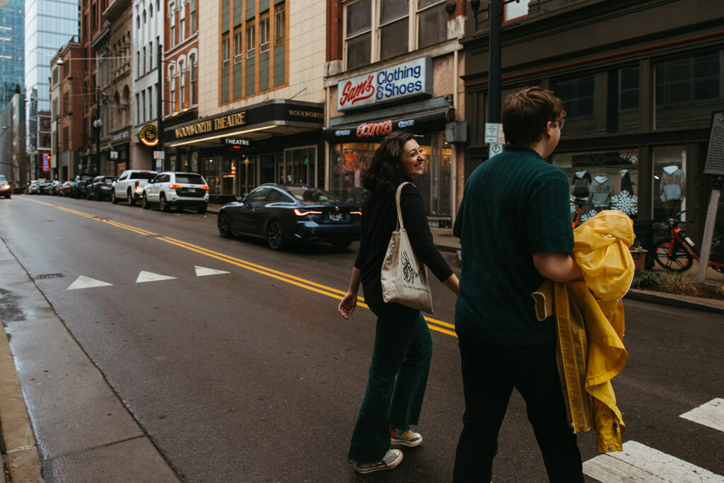 Man carries rain jackets as he walks hand in hand through the streets of downtown Nashville with his fiance