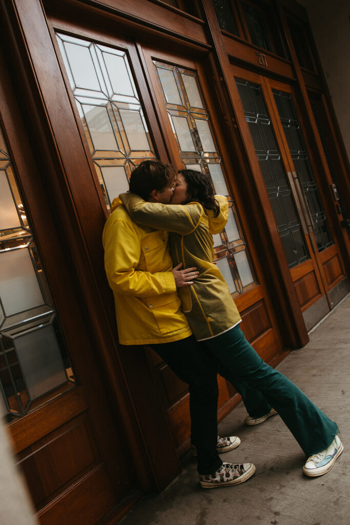 Engaged couple kisses passionately against glass windows in downtown Nashville downpour