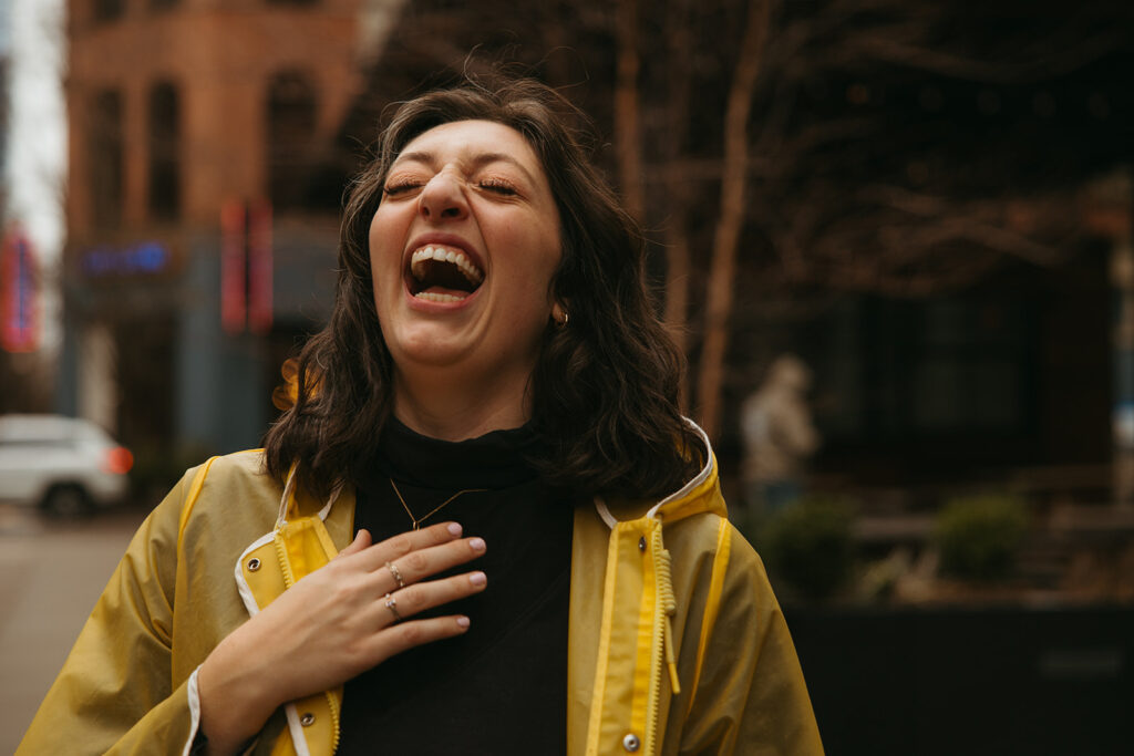 Woman in yellow rain jacket throws her head back in gleeful laughter