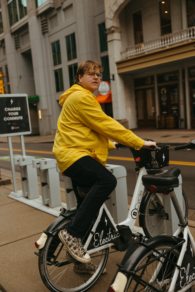 Man in yellow rain jacket climbs on electric bike in downtown Nashville