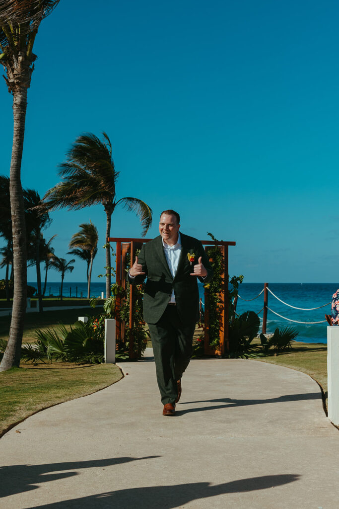 Groom makes his way down the aisle with a backdrop of sheer blue sky and water at destination wedding in Mexico