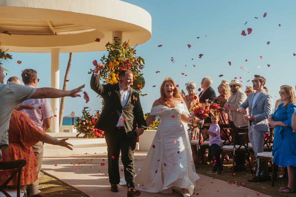 Wedding guests at destination wedding in Mexico throw confetti into the air as newlyweds make their way down the aisle together