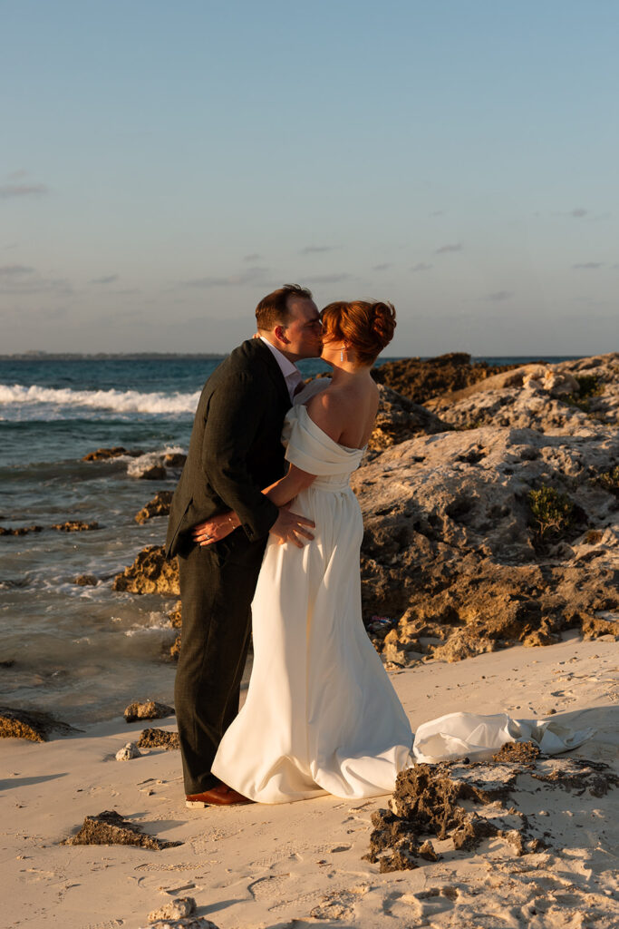 Bride and groom kiss on Cancun cliff overlooking the sea in destination wedding in Mexico