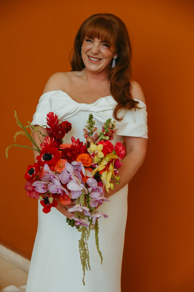 Vibrant bride holds colorful bouquet in front of orange wall