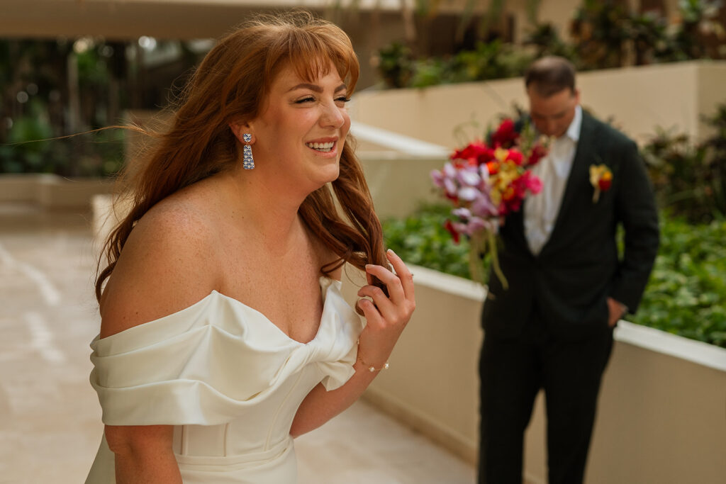 Bride doubles over with laughter in the foreground while groom holds her flowers in the background