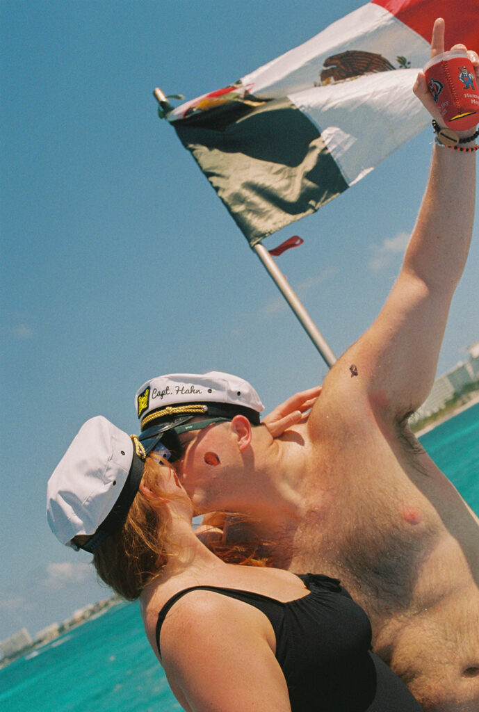 Bride and groom wearing sailor caps on catamaran boat ride kiss