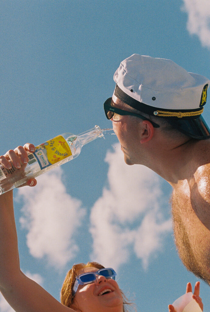 Bride pours custom bottle of liquor into groom's mouth on boat ride at destination wedding in Mexico