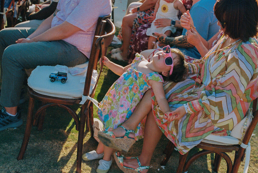 Little girl with pink sunglasses on lays on her mom's lap at destination wedding in Mexico