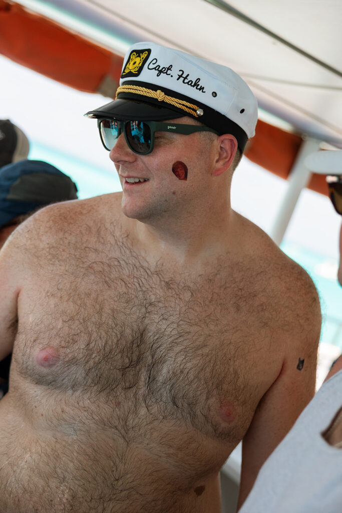 Groom with a sailor cap and sticker tattoo on his face enjoys boat ride in Cancun
