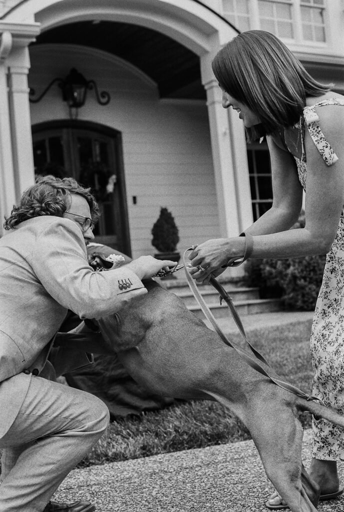 Groom hugging his dog before the ceremony while a guest helps hold him