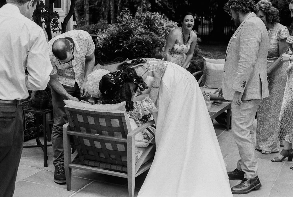 Bride leaning down to hug a guest while others gather during cocktail hour