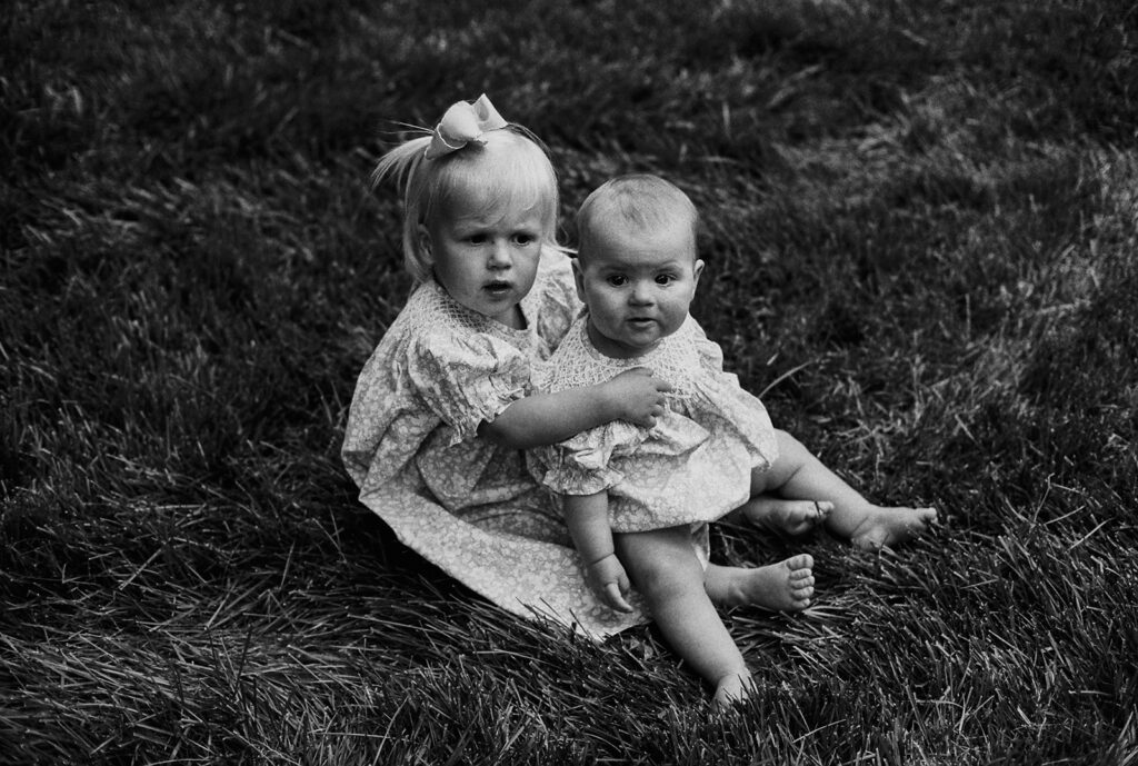 Two toddlers sitting together in the grass during a candid moment at the backyard wedding