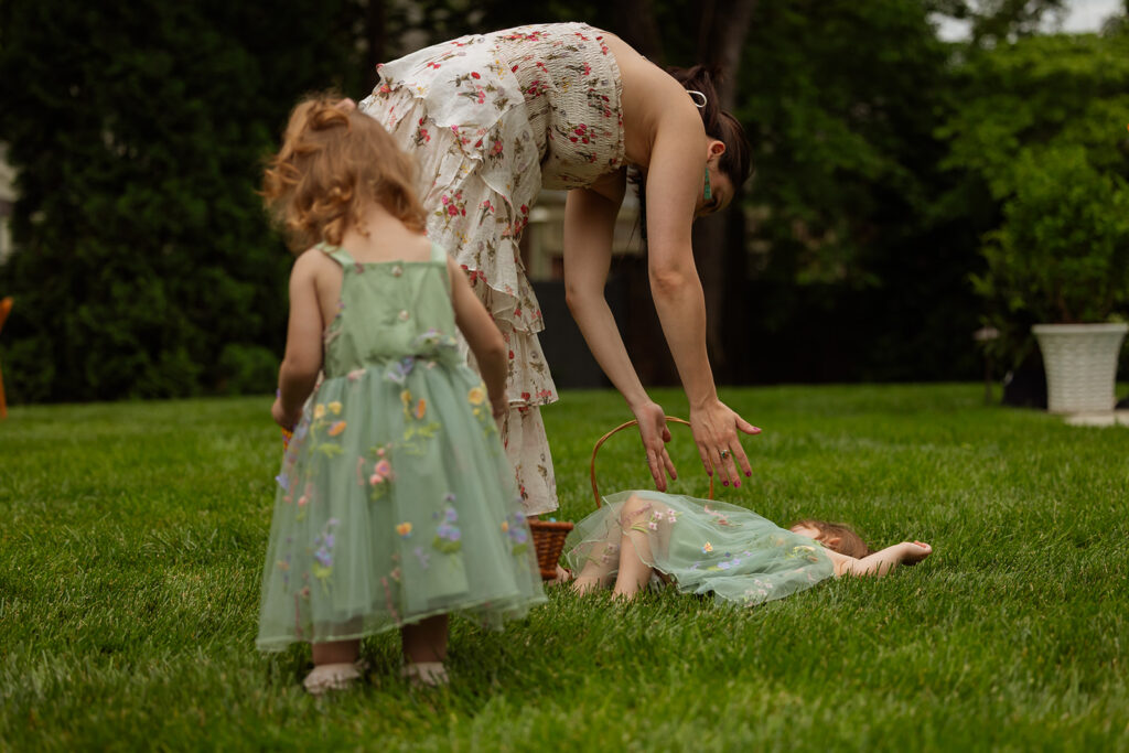 Toddler in a tulle dress lying in the grass as another child and guest look on at a backyard wedding