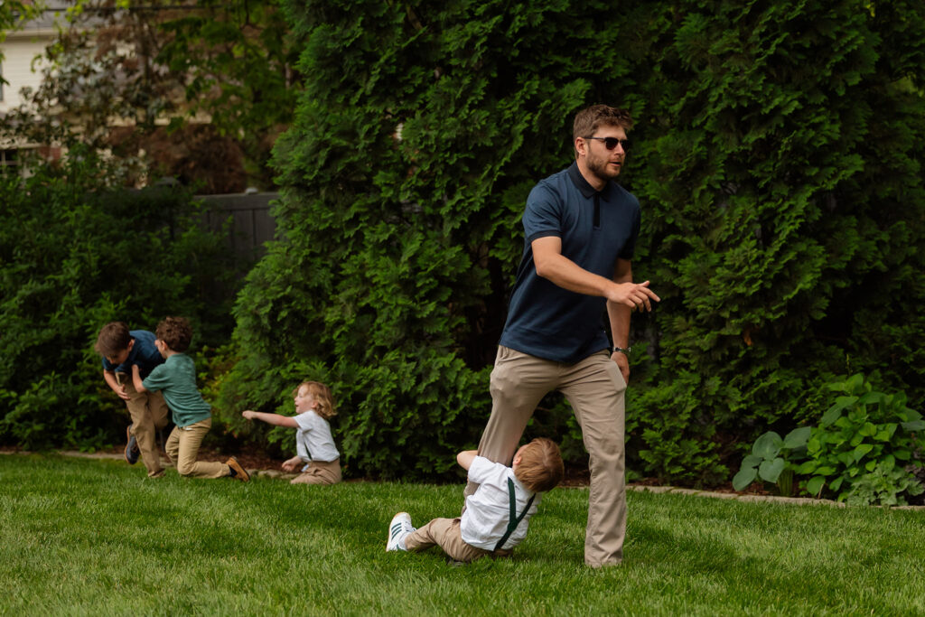 Children sprawled out and play-fighting in the grass during the relaxed backyard wedding celebration
