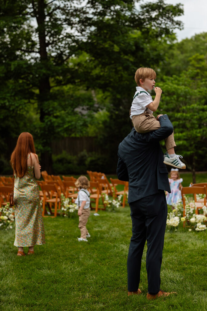 Guest carrying a child across the lawn after the backyard wedding ceremony