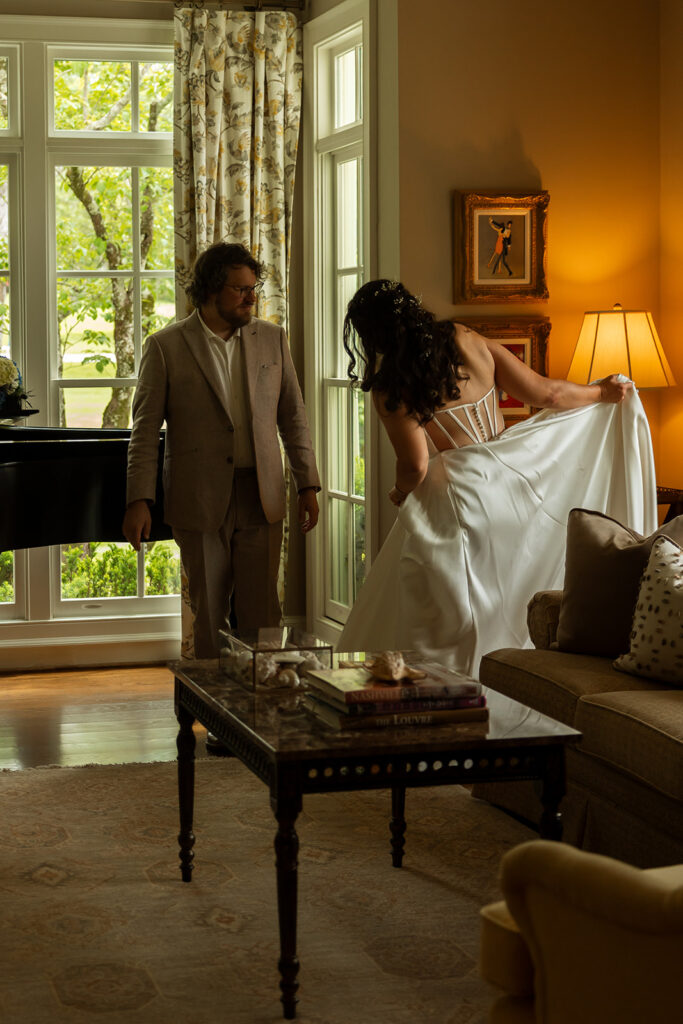 Bride showing off her dress while her husband watches during the getting-ready moments of a backyard wedding