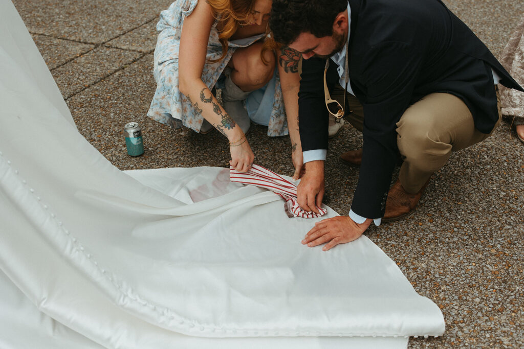 Guests blotting the wine-stained hem of the bride’s dress during the casual backyard wedding
