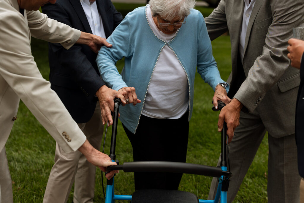 Bride’s grandmother being gently guided across the lawn by family members during the backyard wedding ceremony