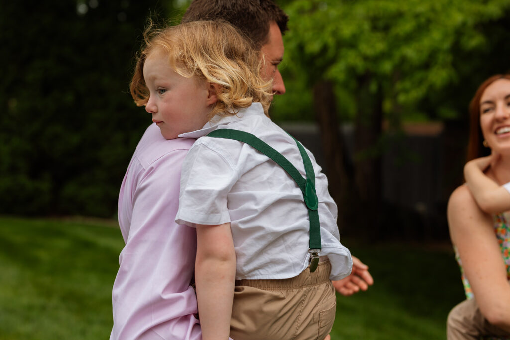 Young boy in suspenders resting his head on a guest’s shoulder
