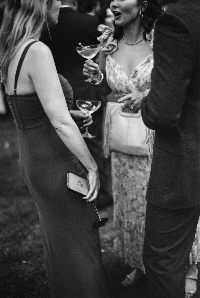 Film wedding photography of guests chatting with cocktails in hand, candid reception detail.