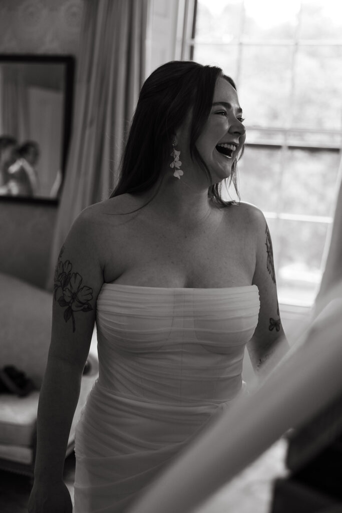 Bride laughing with bridesmaids in golden window light while bouquets are arranged.
