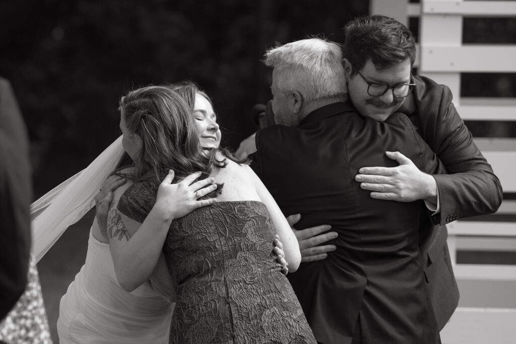 Bride hugging family after the ceremony, joyful candid moment in black and white.