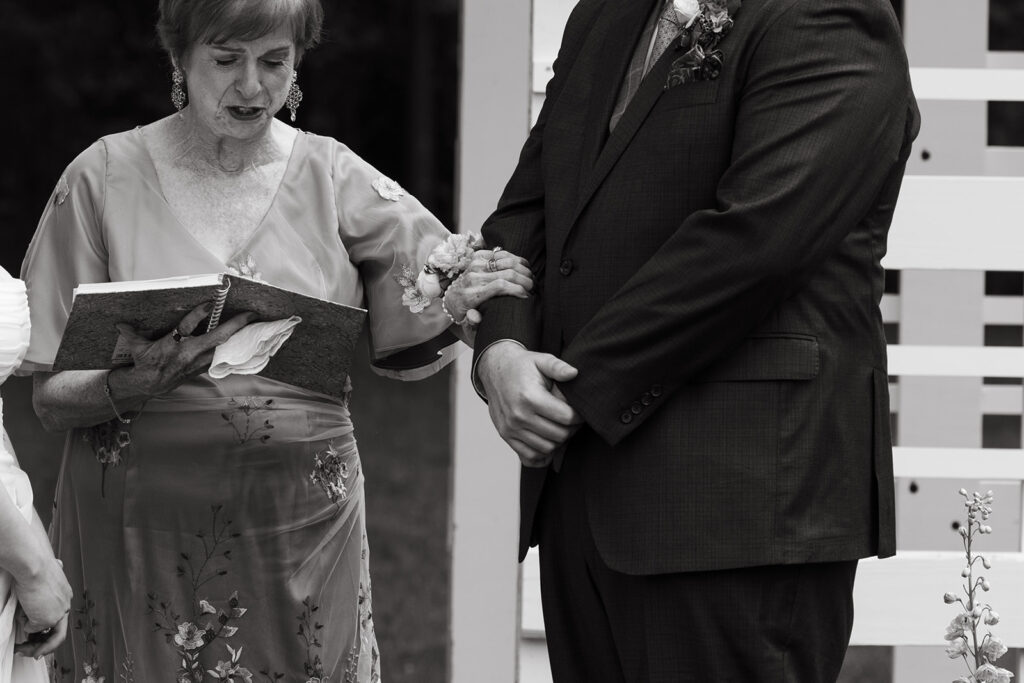 Parent reading from paper during outdoor ceremony, hands trembling with emotion.